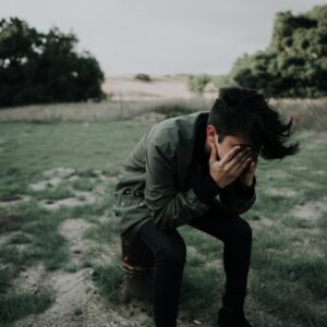 Headache - Man in a green coat in an open field with his head in his hands