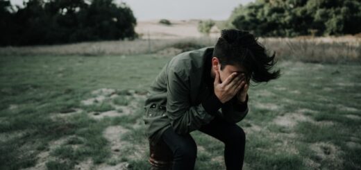 Headache - Man in a green coat in an open field with his head in his hands