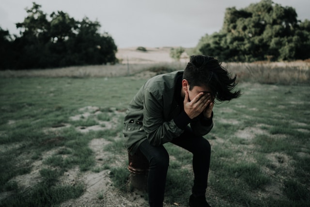 Headache - Man in a green coat in an open field with his head in his hands